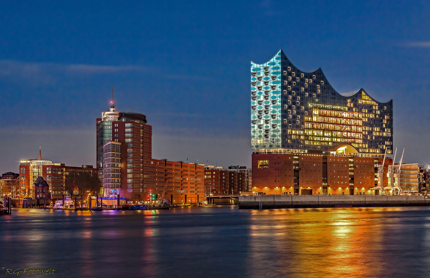 Night view of Hamburg's skyline with the illuminated Elbphilharmonie reflecting on the Elbe River.